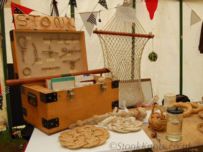 Decorative knotwork and rope craft display by Stonk Knots, including knotting books, a knotboard, hammock, bell pull, kringle mats, Turks Head basket and devil stick with woven Turk's Head grip